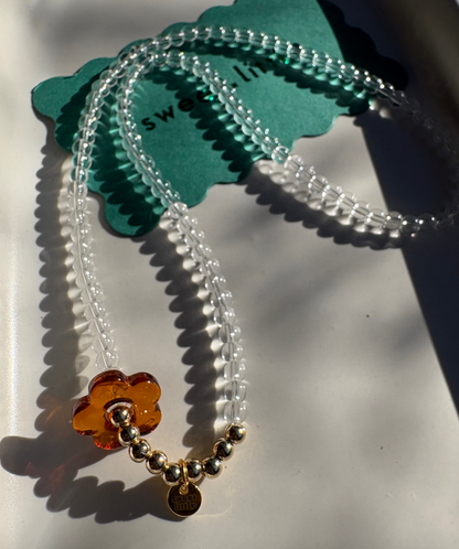 Clear beaded necklace with a brown flower charm on a white surface