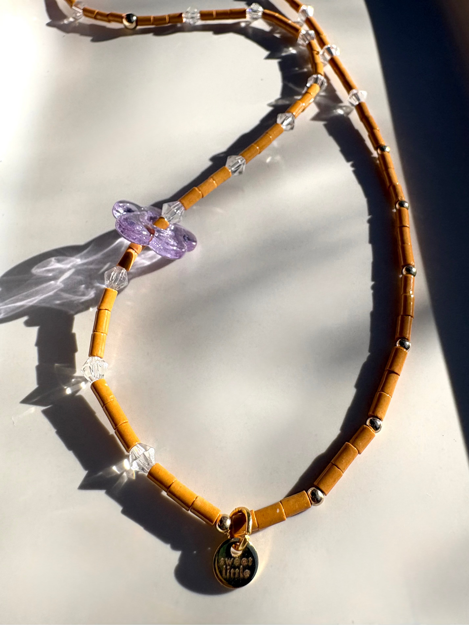 Brown beaded necklace with a purple heart charm on a light surface